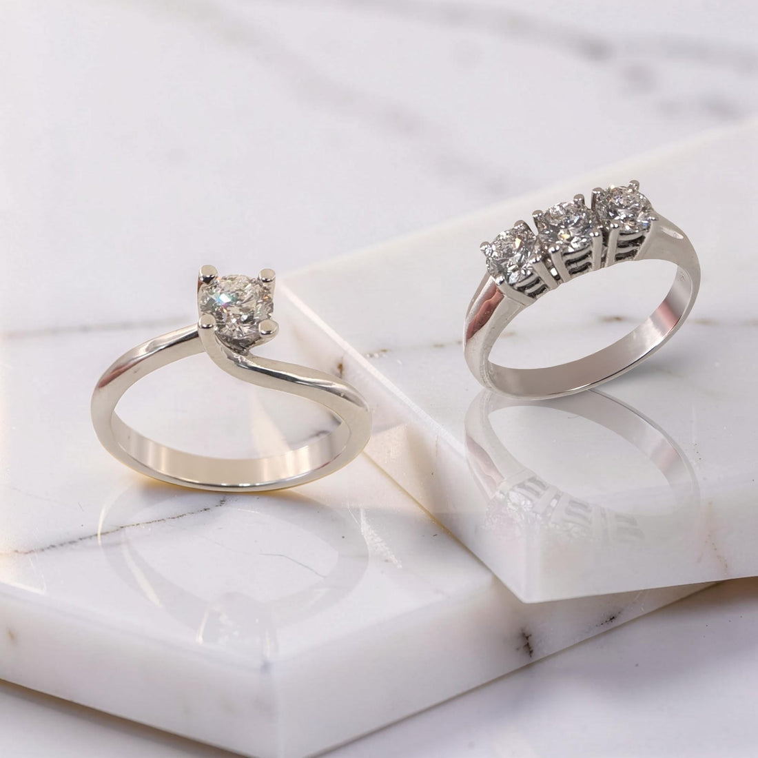 La foto mette in evidenza 2 anelli: un solitario e un Trilogy entrambi gli anelli  montano diamanti naturali certificati GIA D/VS