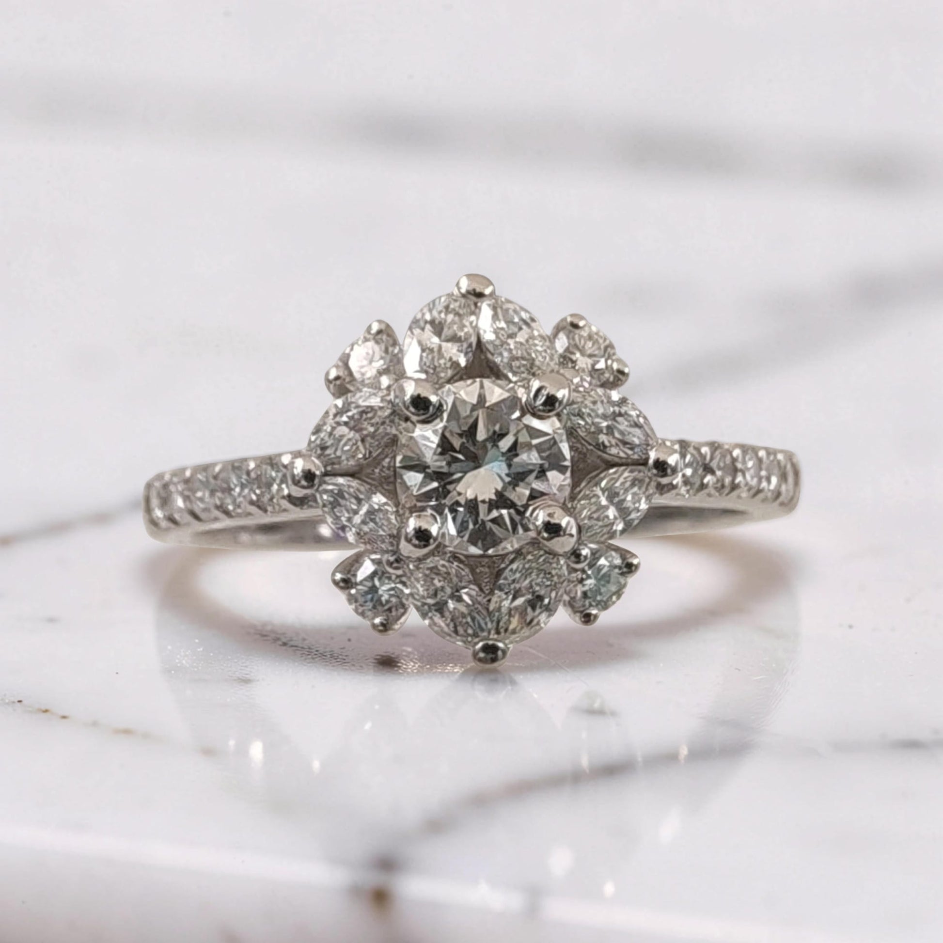 Primo piano di anello in oro bianco 18Kt con diamante centrale taglio brillante da 0,51 ct, circondato da diamanti taglio brillante e marquise disposti a fiore, dettaglio alta gioielleria Meteore Gioielli.