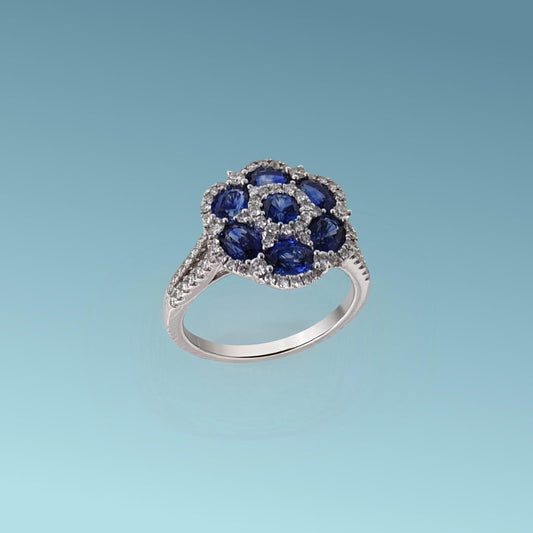 Anello con uno zaffiro blu naturale dal taglio brillante incastonato al centro, circondato da sei zaffiri blu naturali dal taglio ovale per un totale di 2.18 ct, tutti abbracciati da un pavé di diamanti naturali taglio brillante G/VS