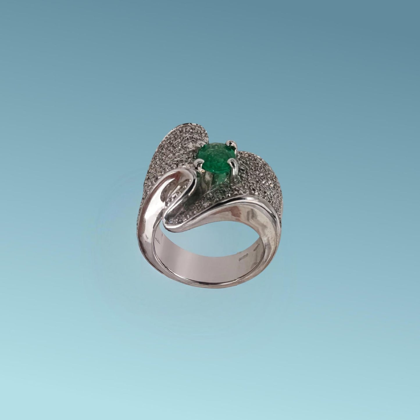 anello in oro bianco 18kt con un design unico impreziosito da un pavè di diamanti naturali taglio brillante g/vs per un totale di 1.36 carati che con il loro movimento sinuoso abbracciano nel centro uno splendido smeraldo naturale taglio ovale di 0.85 carati