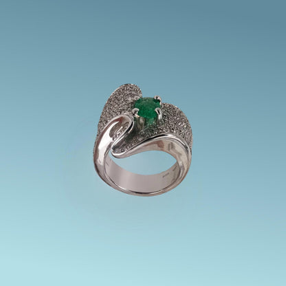 Anello in oro bianco 18kt con un design unico impreziosito da un pavè di diamanti naturali taglio brillante G/VS per un totale di 1.36 carati che con il loro movimento sinuoso abbracciano nel centro uno splendido Smeraldo naturale taglio ovale di 0.85 carati