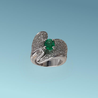 Anello in oro bianco 18kt con un design unico impreziosito da un pavè di diamanti naturali taglio brillante G/VS per un totale di 1.36 carati che con il loro movimento sinuoso abbracciano nel centro uno splendido Smeraldo naturale taglio ovale di 0.85 carati