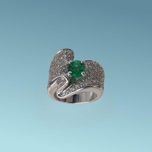 Anello in oro bianco 18kt con un design unico impreziosito da un pavè di diamanti naturali taglio brillante G/VS per un totale di 1.36 carati che con il loro movimento sinuoso abbracciano nel centro uno splendido Smeraldo naturale taglio ovale di 0.85 carati