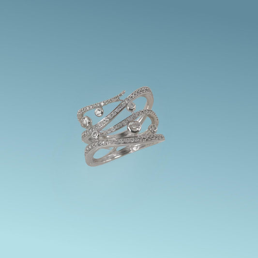 Anello Fantasia in oro bianco 18kt di Meteore Gioielli. La montatura a fascia larga presenta 4 linee sinuose con diamanti naturali incastonati e 6 diamanti incassati su un castone tondo a bordo battuto