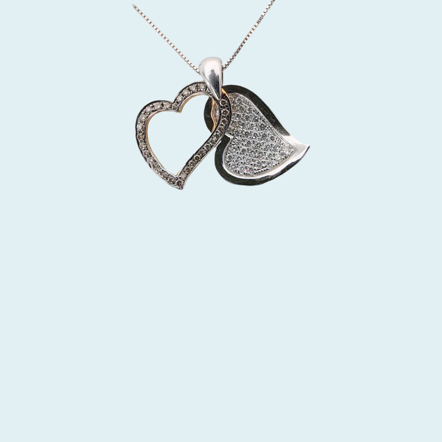 due cuori  sovrapposti, quello superiore in oro rosa incassato con diamanti fancy brown che fa da cornice a quello inferiore in oro bianco con pavè di diamanti. visti separatamente.